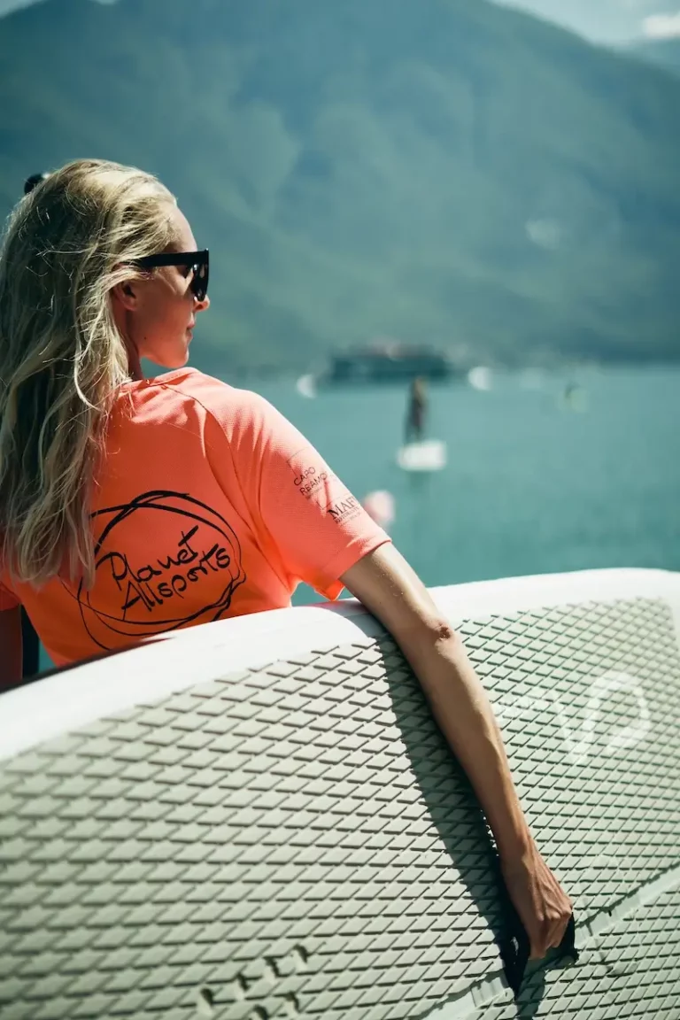 Blonde Frau mit Sonnenbrille trägt SUP-Board am Gardasee