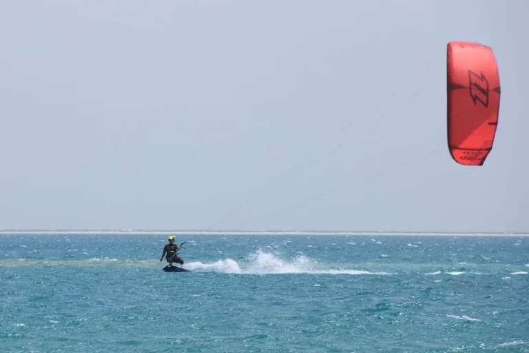 Kitesurfer mit rotem Kite kitet über türkises Wasser in Ägypten