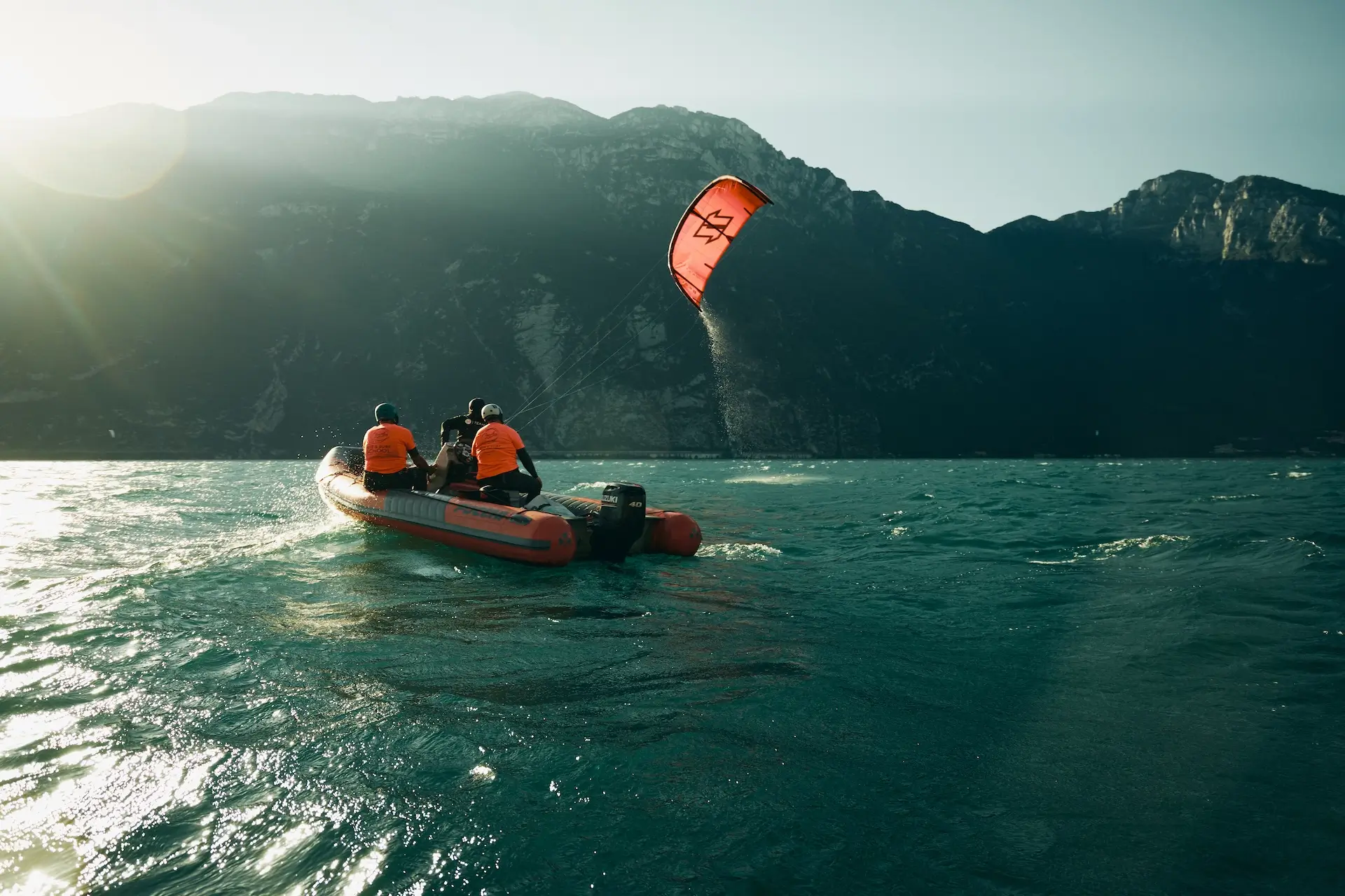 Kitelehrer fliegt roten Kite vom Boot mit zwei Schüler auf dem Boot am Gardasee