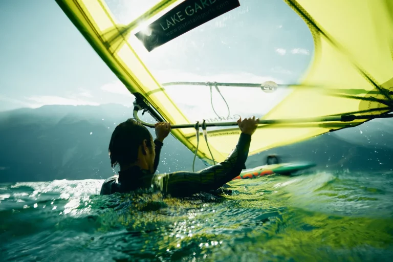 Windsurfer mit gelben Segel macht Wasserstart am Gardasee