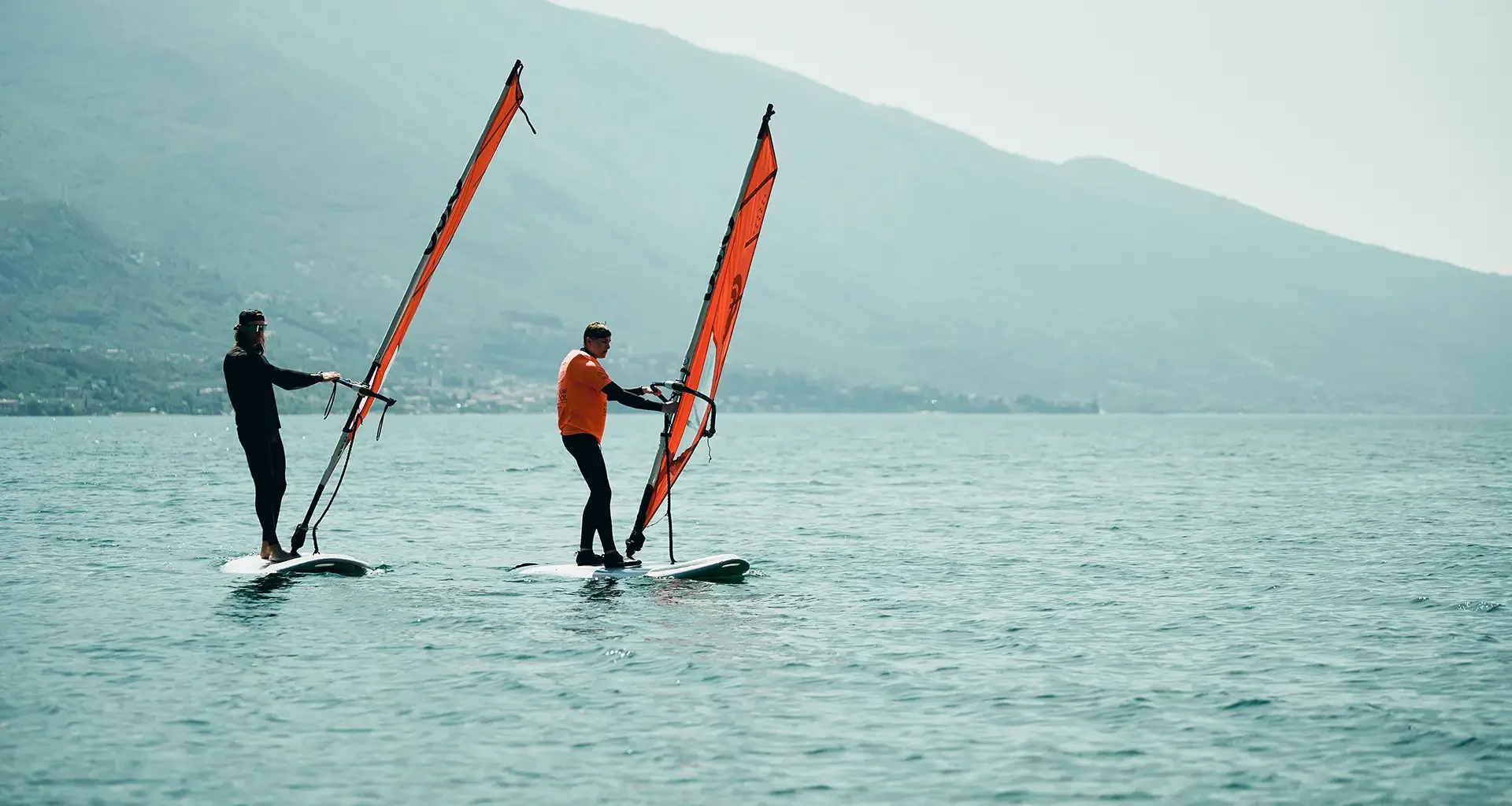 two windsurfers with red sails riding in low wind