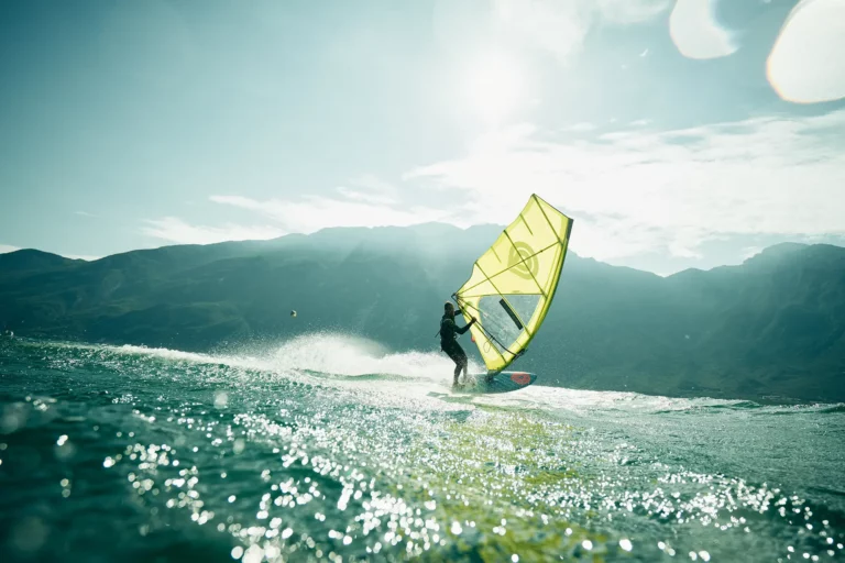 Windsurfer mit gelben Segel bei Gegenlicht macht eine Powerhalse am Gardasee