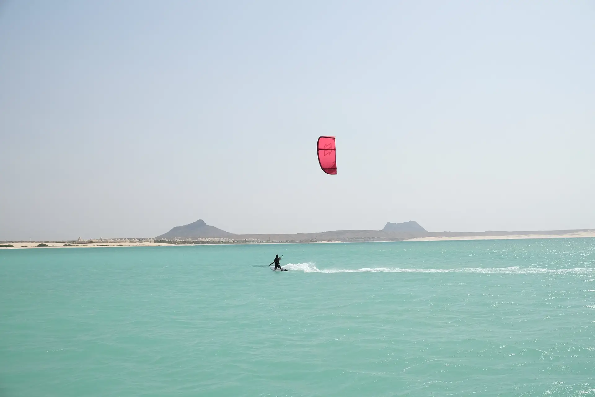 Kiter mit rotem Kite gleitet über türkises Wasser auf Boavista