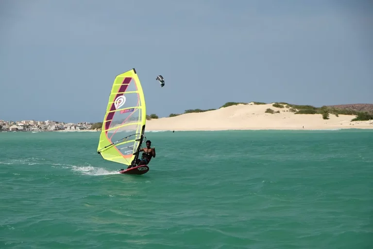 Windsurfer with yellow sail plaining in front of sand dune