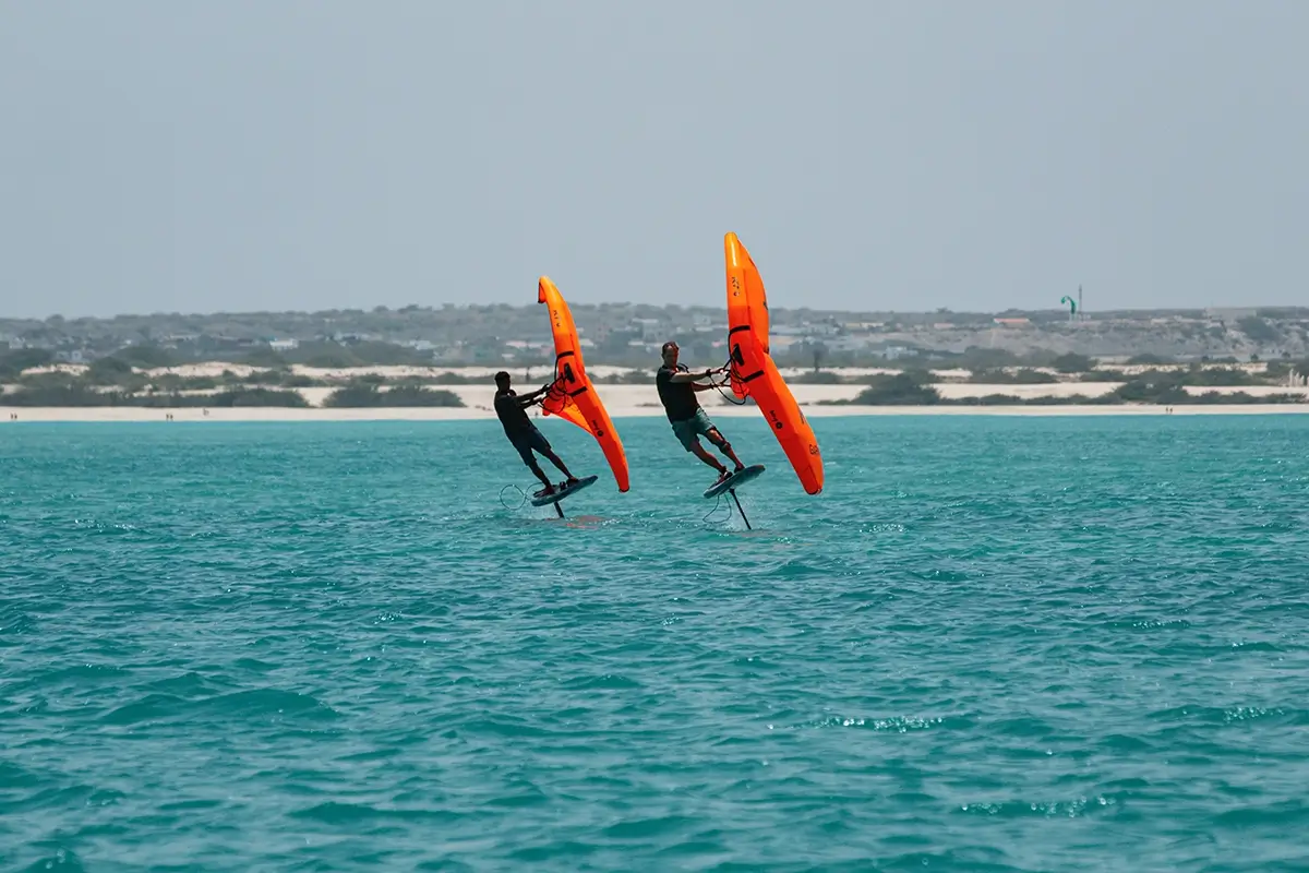 Zwei Wingfoiler mit orangen Wings gleiten über türkises Wasser auf Boavista